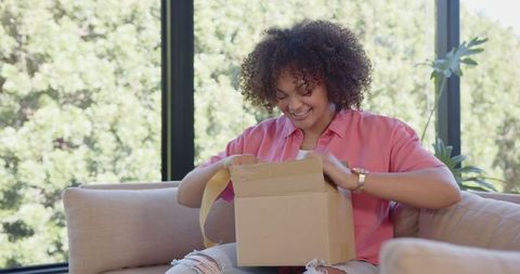 Young woman opening cardboard box on sofa in modern living room