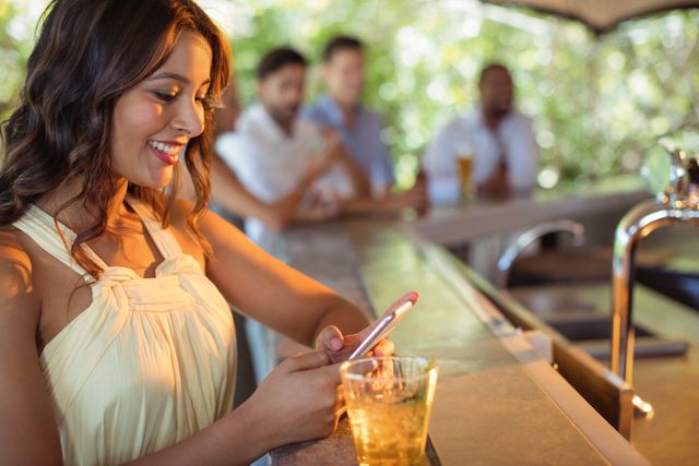Smiling woman using mobile phone while having a glass of beer - Download Free Stock Photos Pikwizard.com