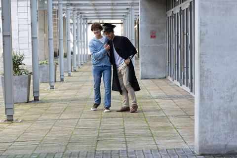 Graduation friends walking arm-in-arm on campus colonnade wearing cap and gown