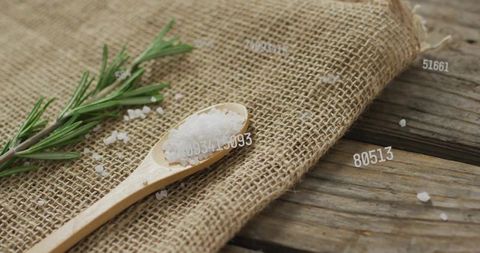 Rustic wooden spoon holding coarse sea salt on burlap with rosemary sprig closeup