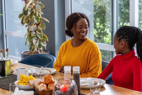 African american mother and daughter sharing joyful breakfast at sunlit dining table