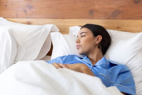 Thoughtful woman relaxing in bed wearing blue pajamas against wooden headboard