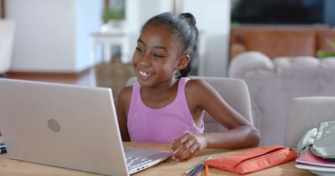African American girl smiling and studying on laptop at home workspace with supplies