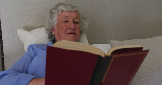 Happy caucasian senior woman at home enjoying reading book sitting up in bed in. at home in isolation during quarantine lockdown.