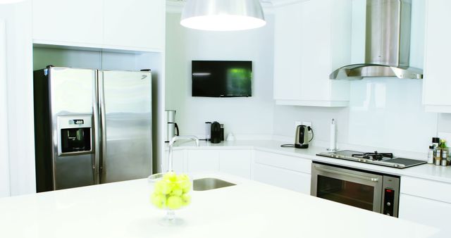 A modern kitchen interior features stainless steel appliances and a bowl of green apples on the island countertop, with copy space. Clean lines and a monochromatic color scheme create a minimalist and sleek design aesthetic.