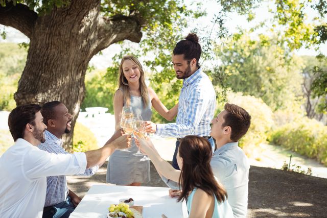 Group of friends raising champagne glasses in a toast at an outdoor restaurant. Ideal for use in content related to social gatherings, celebrations, friendship, leisure activities, and outdoor dining experiences.