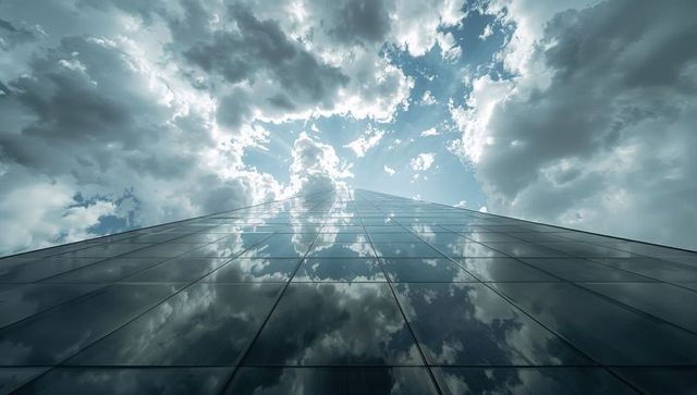Glass facade reflecting dramatic clouds and sunburst from street-level perspective