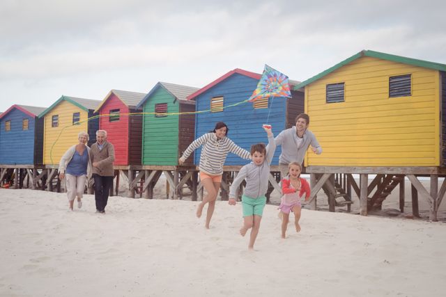 Happy multi-generation family running by beach huts on sand at beach