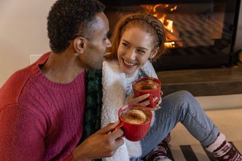 Cozy couple enjoying hot drinks by fireplace on winter evening