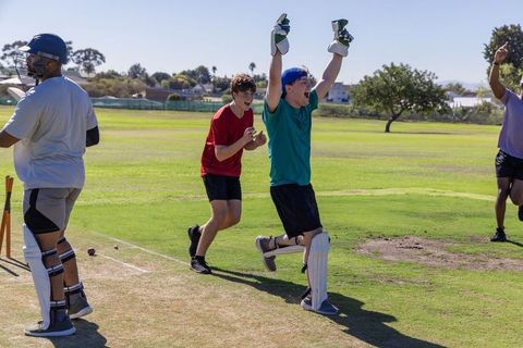 Cricketers celebrating wicket with jubilant wicketkeeper raising gloves on sunny field