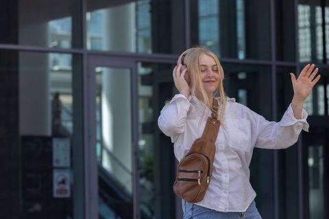 Young woman listening to music with pink headphones outside modern glass office building