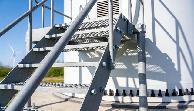 Galvanized grated staircase climbing wind turbine tower on wind farm maintenance pad