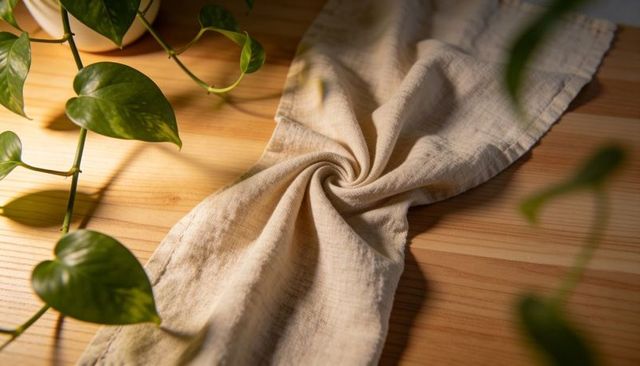 Sunlit linen cloth spiraling on wooden tabletop with pothos vine and warm natural texture
