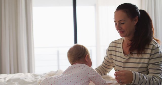 Mother Smiling at Baby Crawling on Bed Near Window - Download Free Stock Images Pikwizard.com