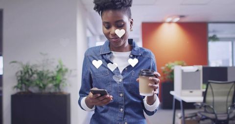 Young woman walking in office checking smartphone and holding coffee with heart overlays