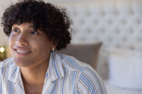 Smiling young man looking upward on cozy tufted bed close-up portrait with warm natural light