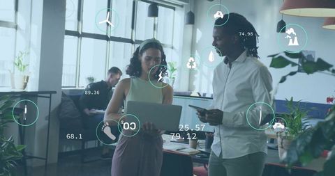 Coworkers using laptop and tablet in modern office with technology interface