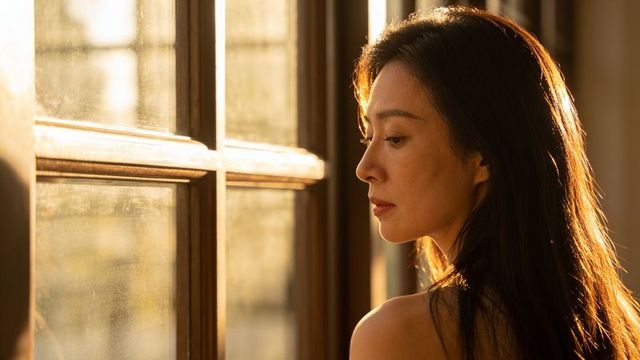 Backlit woman gazing through paned window at home with golden sunlight on hair