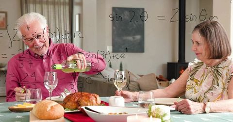 Senior couple enjoying cozy home dinner pouring white wine over roast candlelit ambience