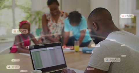 Father working on laptop while mother helping kids study in sunlit home workspace with spreadsheet