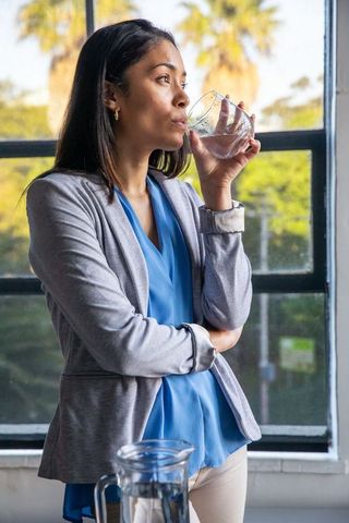 Focused female professional drinking water by window for refreshment
