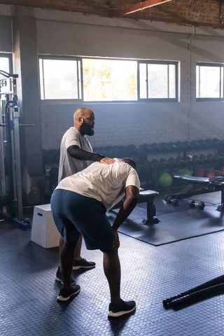 African trainer coaching male athlete catching breath in industrial brick gym