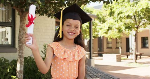 African american girl celebrating school graduation in orange dress holding diploma and mortarboard