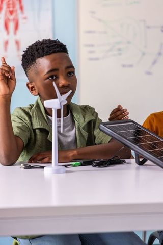 African american preteen raising hand building wind turbine and solar panel in stem classroom