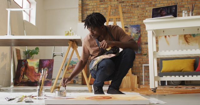 African american male artist wearing apron painting on canvas at art studio. art, hobby and creative occupation concept