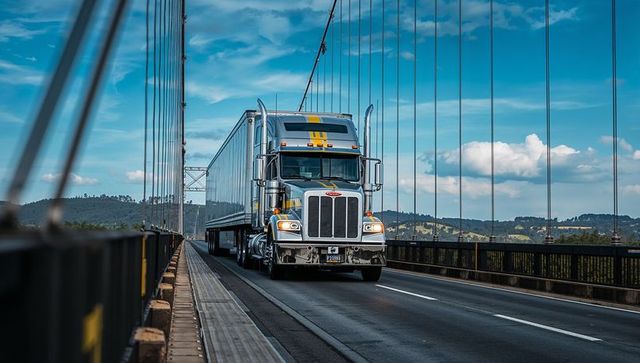 Silver semi truck crossing suspension bridge with yellow stripe and chrome grille