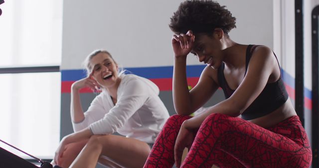 Two women relaxing and laughing after an intense workout in a gym. They are fit and athletic, wearing sportswear. Ideal for use in health and fitness promotions, gym advertisements, wellness programs, and inspirational workout content.
