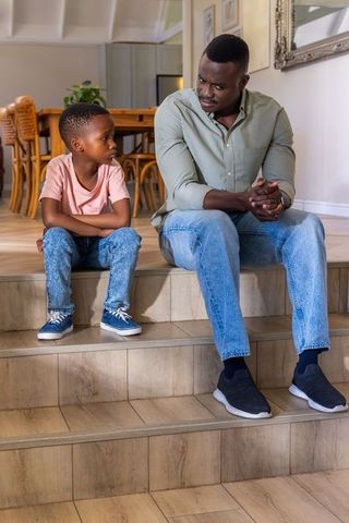 African american father and son having serious conversation on wooden steps at home