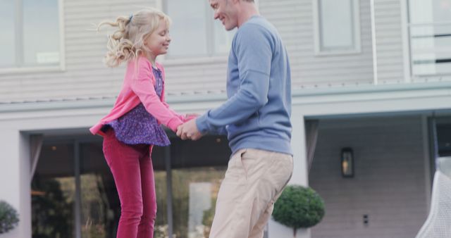 Father and daughter holding hands while playing together in a residential backyard. This image can be used for family-oriented content, advertising parenting products, or promoting outdoor activities.