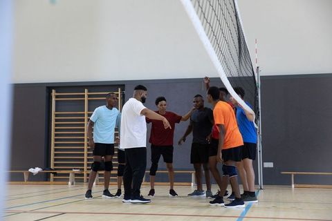 Multicultural male volleyball team gathering for coaching huddle in indoor gymnasium