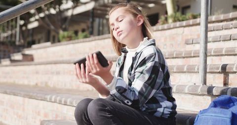 Young Girl Using Smartphone on Sunny Day With Backpack Near School