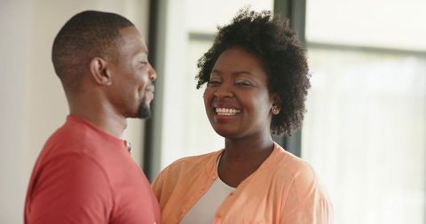 African american couple smiling and embracing in sunlit home, candid lifestyle moment