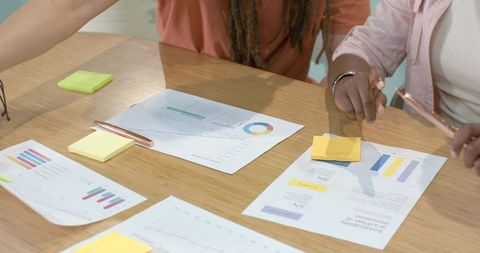 African american colleagues reviewing business charts and sticky notes at office table