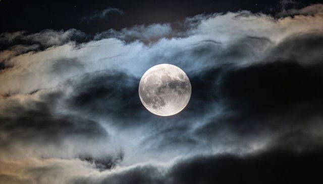 Shining Full Moon Revealing Crater Details Through Layered Clouds and Starry Sky