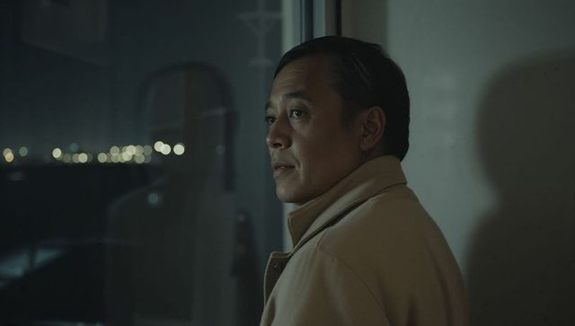 Man standing gazing out window at night with city lights reflection and moody vibes