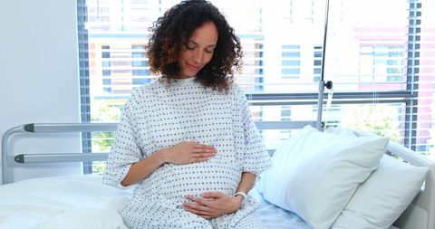 Pregnant Woman Sitting in Hospital Ward Holding Belly
