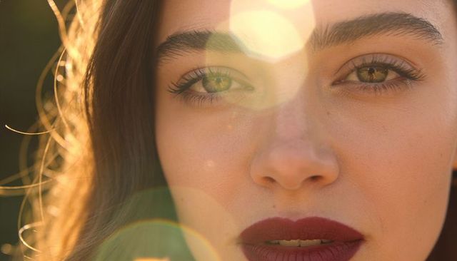 Backlit golden-hour closeup of woman with red lipstick and natural glow with lens flare