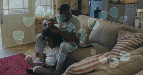 African american father grooming daughter hair while child using tablet for learning