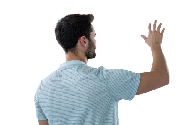 Man standing with back facing camera, arm raised as if interacting with something unseen. Useful for concepts involving virtual reality, technology, interaction, or imaginative scenarios.