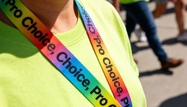 Close-up rainbow pro choice lanyard on neon shirt at outdoor rally, bright colors