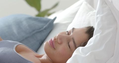 Smiling Young Woman Relaxing in Morning Light in Cozy Bedroom