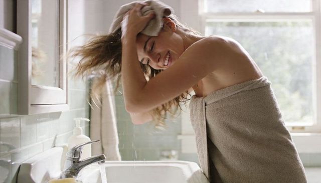 Smiling woman drying wet hair with towel in sunlit bathroom morning self care routine