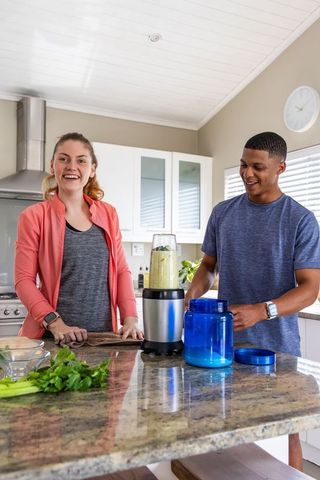 Happy couple preparing green smoothie on granite kitchen island, blending healthy nutrition routine