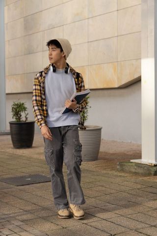 Asian student walking on campus plaza carrying notebooks wearing headphones and beanie