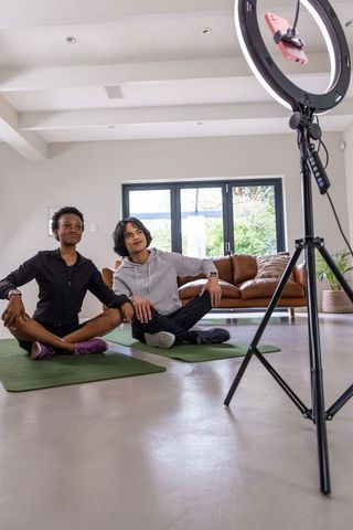Diverse friends leading home yoga session on mats recording with ring light and tripod