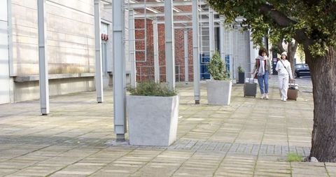 Two travelers walking with rolling luggage on urban tiled plaza wearing coats and scarves